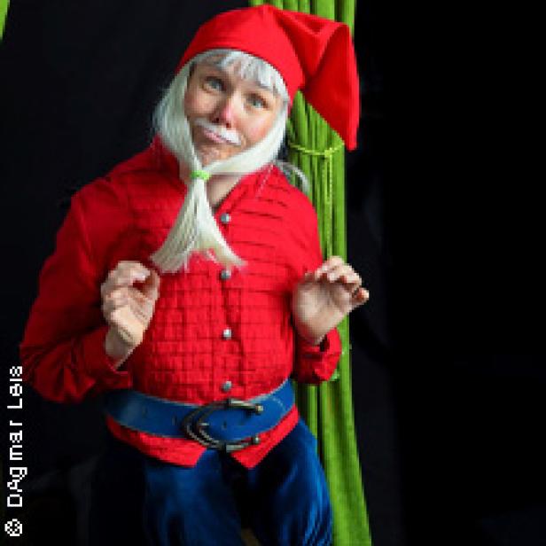 Eine Person in einem roten Kostüm und einer Zipfelmütze mit einem weißen Bart und Schnurrbart.