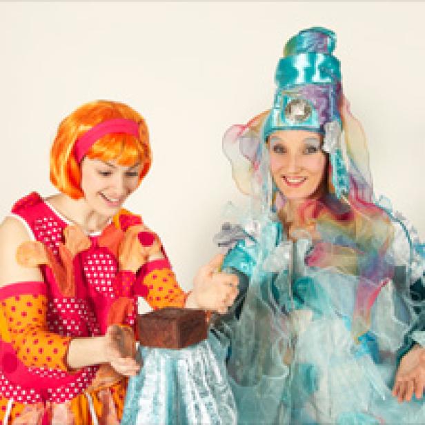 Zwei Frauen in bunten Kostümen präsentieren einen Schokoladenkuchen.