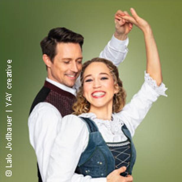 Ein lächelndes Paar in Tracht posiert vor einem grünen Hintergrund.