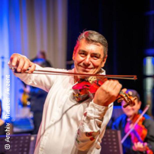 Ein lächelnder Mann spielt auf einer Bühne Geige.