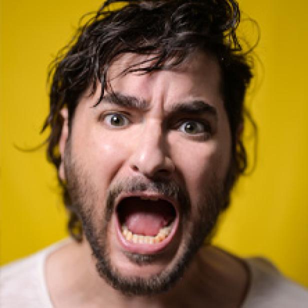 Ein Mann mit Bart und weit geöffnetem Mund blickt in die Kamera.