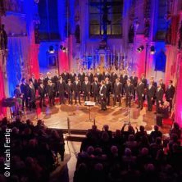 Ein großer Chor tritt in einer Kirche vor Publikum auf, beleuchtet in Rot und Blau.
