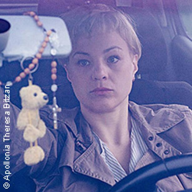 Eine Frau mit kurzem blonden Haar sitzt in einem Auto.