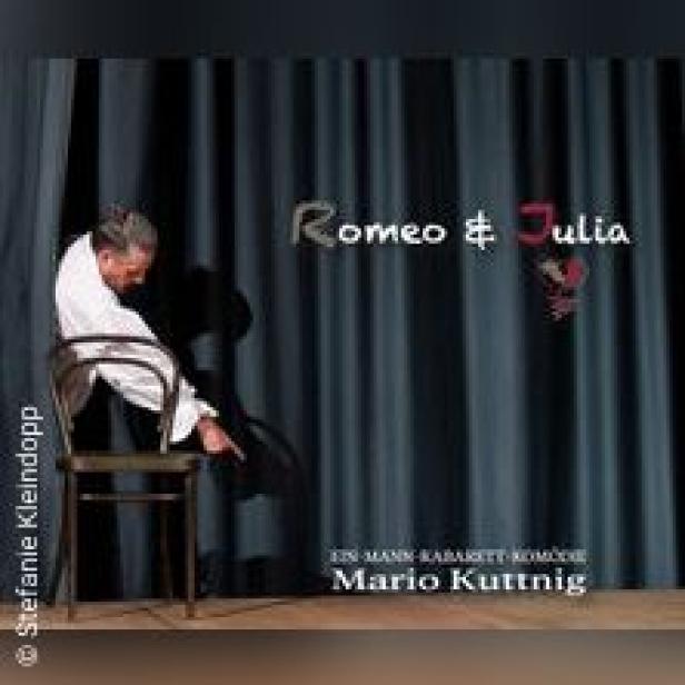 Ein Mann sitzt auf einem Stuhl vor einem Vorhang mit dem Titel „Romeo & Julia“.