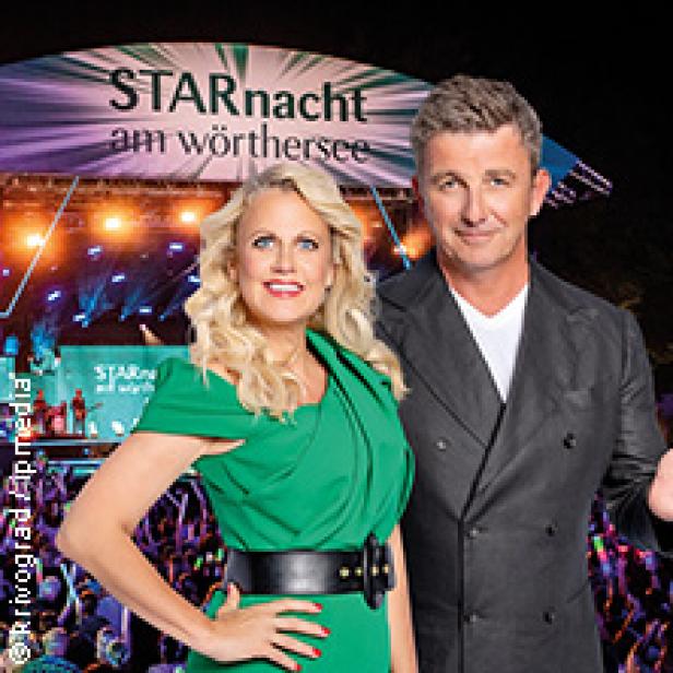 Moderator Barbara Schöneberger und ein Mann posieren vor der Bühne der „Starnacht am Wörthersee“.