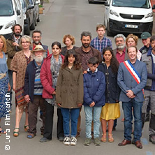 Eine Gruppe von Menschen steht auf einer Straße vor geparkten Autos.