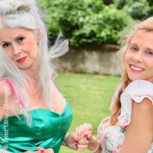 Zwei Frauen halten Händchen und lächeln in die Kamera.