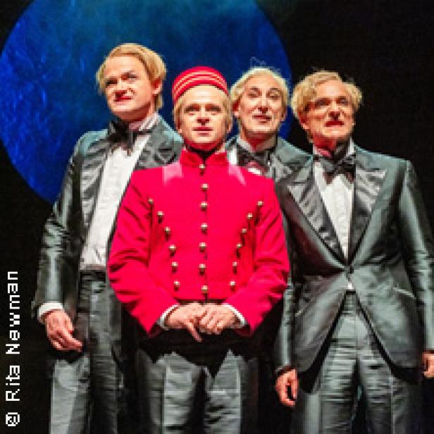 Vier Männer in Kostümen stehen auf einer Bühne.