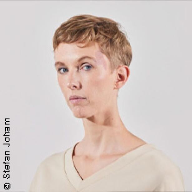 Porträt einer jungen Frau mit kurzen blonden Haaren und hellblauer Kleidung.