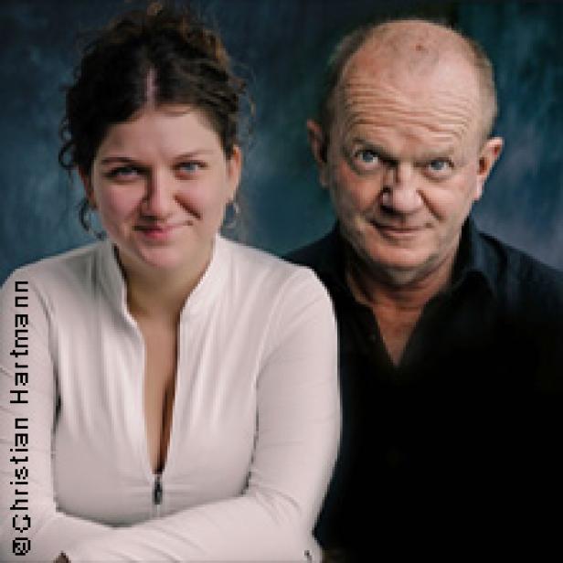 Ein Porträt einer jungen Frau und eines älteren Mannes vor einem dunklen Hintergrund.