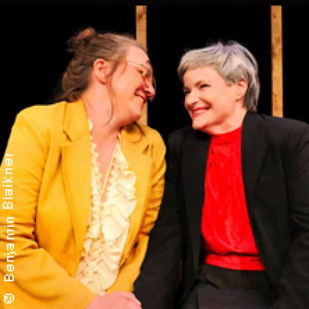 Zwei Frauen sitzen einander zugewandt und lächeln sich an.