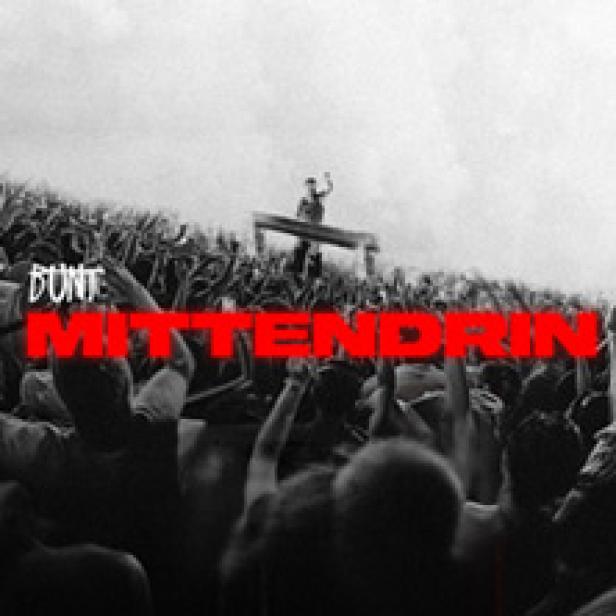 Eine Menschenmenge jubelt vor einer Bühne inmitten eines Feldes.