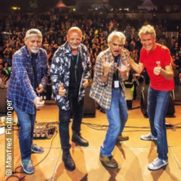 Eine Band posiert auf einer Bühne vor Publikum.