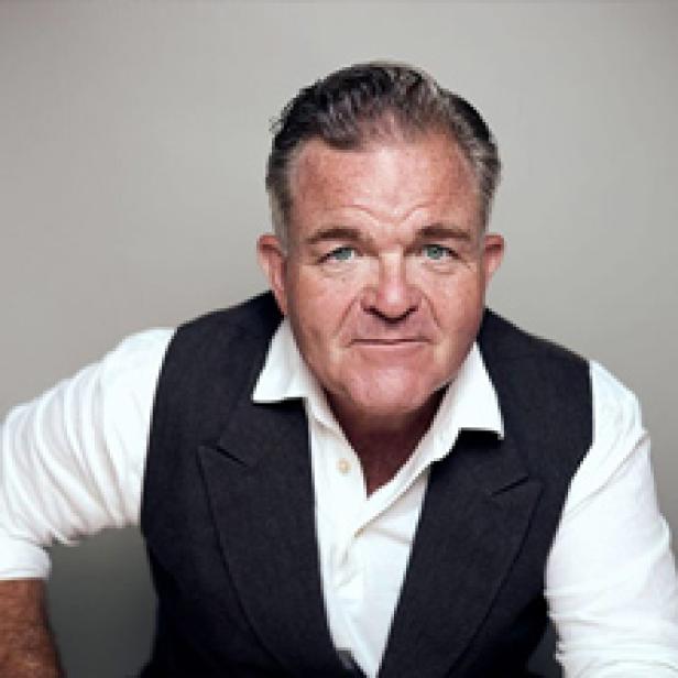 Porträt eines Mannes mit weißem Hemd und dunkler Weste vor einem grauen Hintergrund.