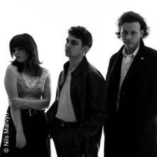 Schwarzweißaufnahme von drei Personen, die nebeneinander stehen.