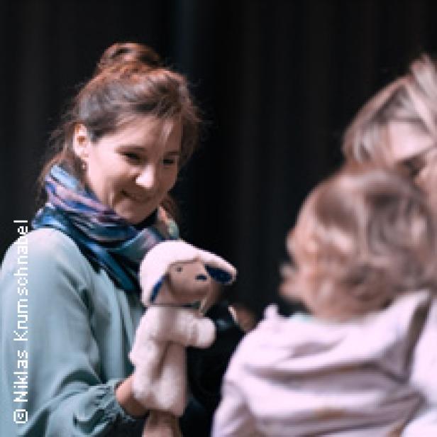 Eine Frau hält ein Stofftier in der Hand und lächelt ein Kind an.