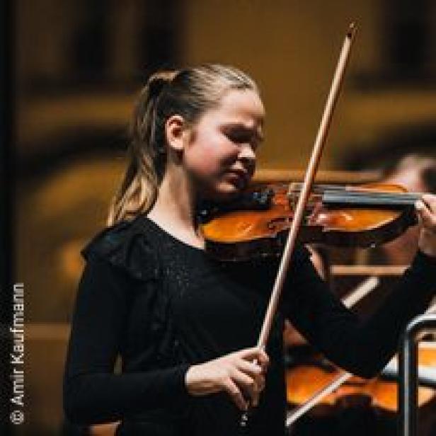 Ein junges Mädchen spielt Violine in einem Orchester.