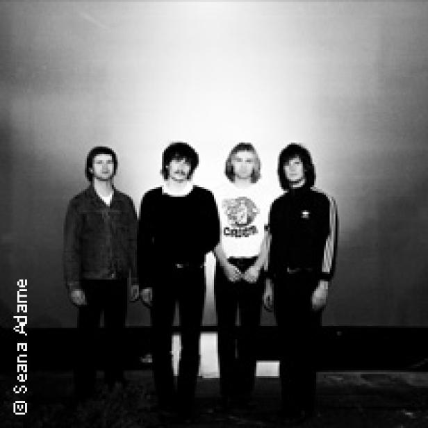 Die Band The Motors posiert vor einer Wand.