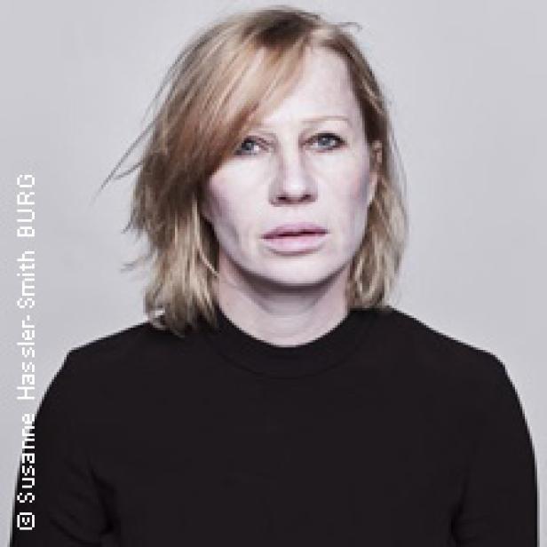 Porträt einer Frau mit blonden, schulterlangen Haaren und einem schwarzen Oberteil.