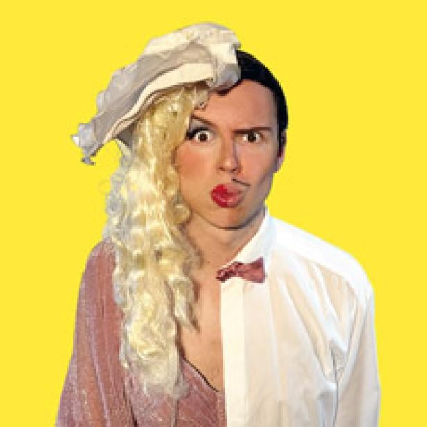 Ein Mann mit Make-up und einer Perücke, zur Hälfte in Damen- und zur Hälfte in Herrenkleidung gekleidet.