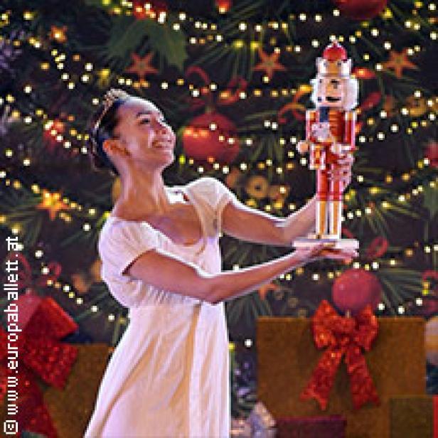 Eine Ballerina hält einen Nussknacker vor einem Weihnachtsbaum.