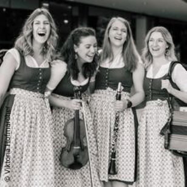 Vier Frauen in Dirndln lachen und halten Musikinstrumente.